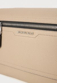 Beige tekstureret læderclutch med en sølvfarvet lynlås og et fremtrædende logo. Har fine syninger og et slankt, minimalistisk design.