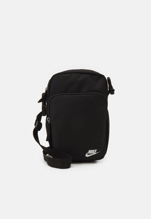 Lille sort Nike skuldertaske med frontlynlåslomme og justerbar rem på en ensfarvet hvid baggrund.