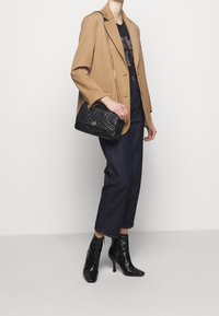 Brązowa marynarka na czarnej koszulce z nadrukiem, zestawiona z ciemnymi, skróconymi spodniami denimowymi i czarnymi botkami z ostrym czubkiem. Czarna pikowana torebka na ramię.