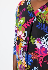 Multifärgad blommig blus med svart bakgrund, med V-ringning, trekvartslånga ärmar och invecklade mönster i blått, rosa, grönt och gult.