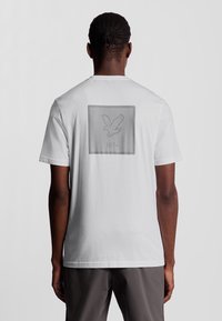 Hvid bomulds t-shirt med et tekstureret firkantet design og en fuglesilhuet samt "1874" trykt i midten på bagsiden.