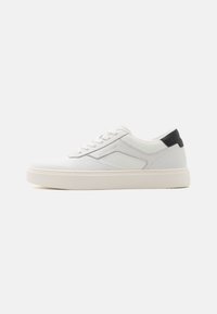 Sneaker bianca con tomaia testurizzata e dettagli lisci, con un tab sul tallone nero, chiusura con lacci e una suola spessa bianca.
