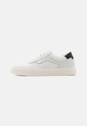 Sneaker bianca con tomaia testurizzata e dettagli lisci, con un tab sul tallone nero, chiusura con lacci e una suola spessa bianca.