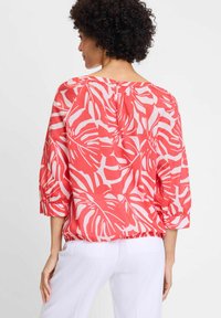 Rot-weiße Bluse mit einem Blättermuster, Dreiviertelärmel und einem gerafften Saum. Knopfverschluss auf der Rückseite verleiht Details.