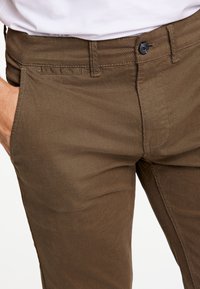 Hnědé bavlněné kalhoty s texturovaným povrchem, předními kapsami a zipem s jedním knoflíkem.