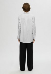 Camicia a righe bianche e grigie con maniche lunghe, polsini abbottonati e una vestibilità rilassata, abbinata a pantaloni neri larghi.