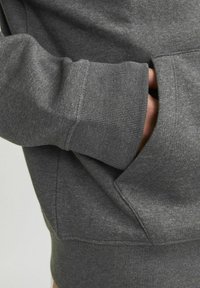 Sudadera gris con tejido texturizado, equipada con puños de canalé y un bolsillo tipo canguro. Primer plano de la manga izquierda y el bolsillo.