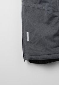 Graue Stoffjacke mit glatter Oberfläche, ausgestattet mit einem Reißverschluss am Saum, elastischem Bund und einem kleinen Logotag an der Seite.