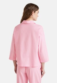 Conjunto de pijama a rayas rosas que incluye una camiseta de manga corta con cuello y pantalones a juego, fabricado con un tejido suave y de textura lisa.