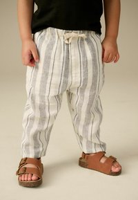 Leichte, gestreifte Baumwollhosen mit einem Kordelzug-Bund, kombiniert mit braunen Sandalen, die zwei verstellbare Riemen und eine Korksohle haben.