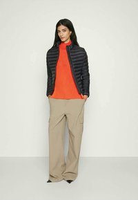 Black puffer jacket over an orange ribbed sweater, paired with beige wide-leg pants. The outfit features clean lines and a contemporary silhouette.