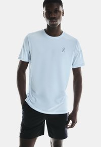 Lichtblauw atletisch shirt met korte mouwen en een ronde halslijn, met een klein grijs logo op de borst, gecombineerd met zwarte shorts. Soepele textuur.