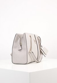 Sac en cuir de couleur gris clair avec une forme structurée, des accents en chaîne et un motif embossé. Il dispose d'une fermeture zippée et d'une étiquette amovible.