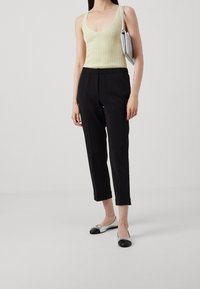 Débardeur côtelé jaune pâle, pantalon noir fuselé avec poignets, et chaussures plates noir et argent, accompagnés d'une pochette argentée.