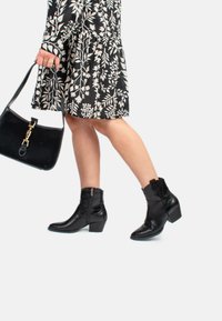 Botas negras hasta el tobillo con un patrón texturizado parecido al cuero de cocodrilo, un tacón bajo y cremallera lateral. Combinadas con un vestido de estampado floral y un bolso.