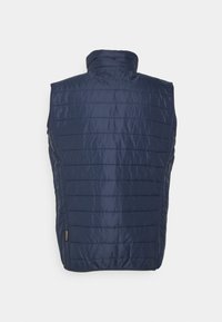 Marineblaue isolierte Weste, ärmellos mit hohem Kragen, mit diagonaler Steppung und einem kleinen Markierungslabel am Saum.