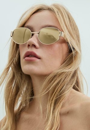 Sonnenbrille mit goldfarbenem Rahmen und ovalen, reflektierenden Gläsern. Dünne, metallische Bügel und minimalistisches Design. Ausgewogene Proportionen und glatte Textur.