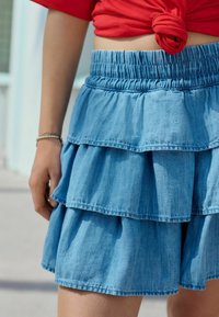 Denim tiered nederdel i lyseblå med elastisk talje. Har tre lag med rynk og en blød tekstur.