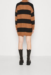 Abito maglione a maglia con righe orizzontali nere e marroni, design con colletto alto e maniche lunghe. Abbinato a stivali platform neri alti.