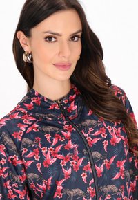 Marineblå zip-up jakke med blomster- og dyreprint i rød og pink, med høj krave og glat, tekstureret materiale.