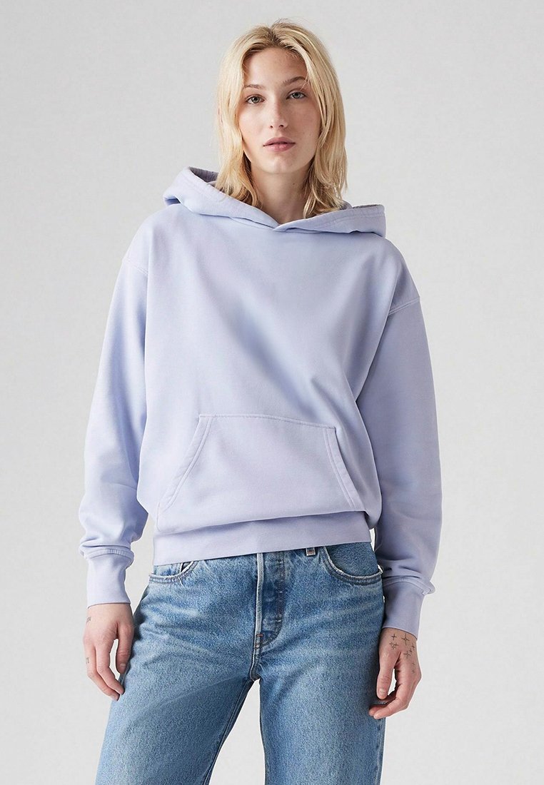 Hoodie viola chiaro realizzato in tessuto morbido; presenta una tasca frontale, cappuccio con cordino e polsini a coste. Indossato con jeans in denim blu.