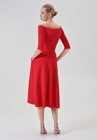 Rotes, knielanges Kleid mit Dreiviertelärmeln, schulterfreiem Ausschnitt und seitlichen Taschen. Glatte Textur und taillierter Oberteil.