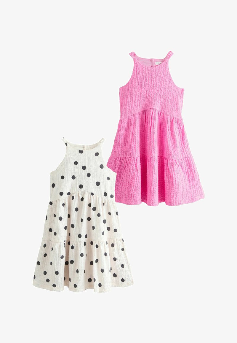 Deux robes en coton sans manches à volants pour filles : une rose unie, l'autre blanche à pois noirs, toutes deux en tissu texturé.