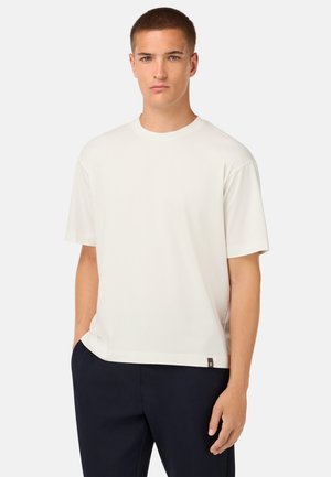T-shirt bianco a maniche corte realizzato in tessuto liscio con scollatura a girocollo e un piccolo badge del logo sull'orlo, abbinato a pantaloni scuri.