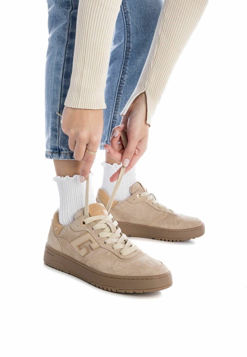Baskets en suède beige avec une finition texturée, semelle en caoutchouc et lacets beiges, associées à des chaussettes blanches en maille côtelée.