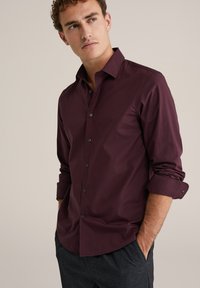 Bordo ilgomis rankovėmis marškiniai, pagaminti iš lygaus audinio, su smailiu apykakle, sagčių užsegimu priekyje ir sukabintomis rankovėmis su juodomis sagomis.