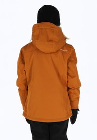 Orange wasserdichte Jacke mit Kapuze, elastischen Bündchen und glatter Textur. Darüber sichtbar, eine schwarze Strickmütze, passend mit Handschuhen.