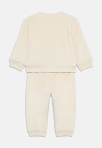 Ensemble beige en deux pièces en tissu ribbé. Le sweat-shirt a des manches longues et un col rond ; le pantalon possède une taille élastique et des jambes fuselées.