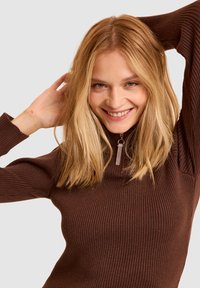 Maglione a collo alto marrone a coste con dettaglio con zip sul collo. Il tessuto ha una finitura texturizzata, design aderente e maniche lunghe.