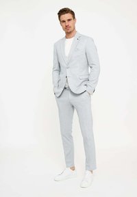 Lichtgrijs pak van gladde stof, met een enkelvoudige blazer en op maat gemaakte broeken, gecombineerd met een wit T-shirt en witte sneakers.
