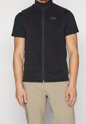 Homme portant une veste polaire noire sans manches zippée sur un t-shirt noir et un pantalon cargo beige, debout, les bras détendus le long du corps.