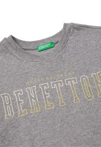 Šedé bavlněné tričko s kulatým výstřihem. Na přední straně se nachází text "UNITED COLORS OF BENETTON" v tučném žlutém písmu.
