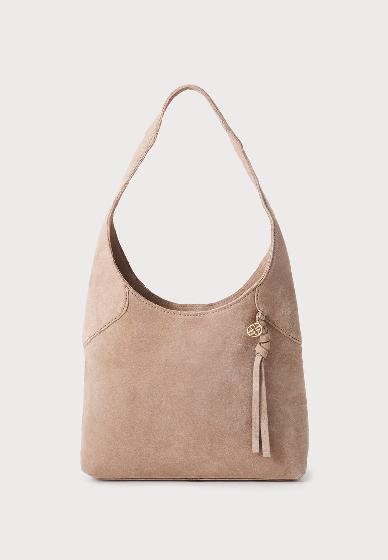 Sac bandoulière en daim beige avec une seule large bandoulière et un pendentif pompon suspendu à un petit anneau doré sur le devant.