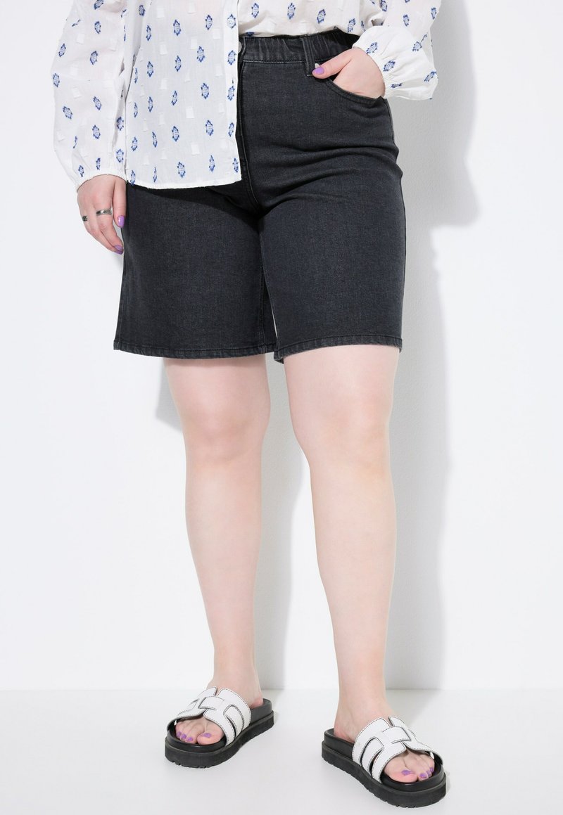 Zwarte denimshorts met een elastische tailleband, een rechte snit, en zijzakken, gecombineerd met witte slidesandalen met zwarte zolen.