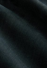 Textielstof in donkergroen, zachte textuur met een subtiel geweven patroon, waarop plooien en een lichte glans zichtbaar zijn.
