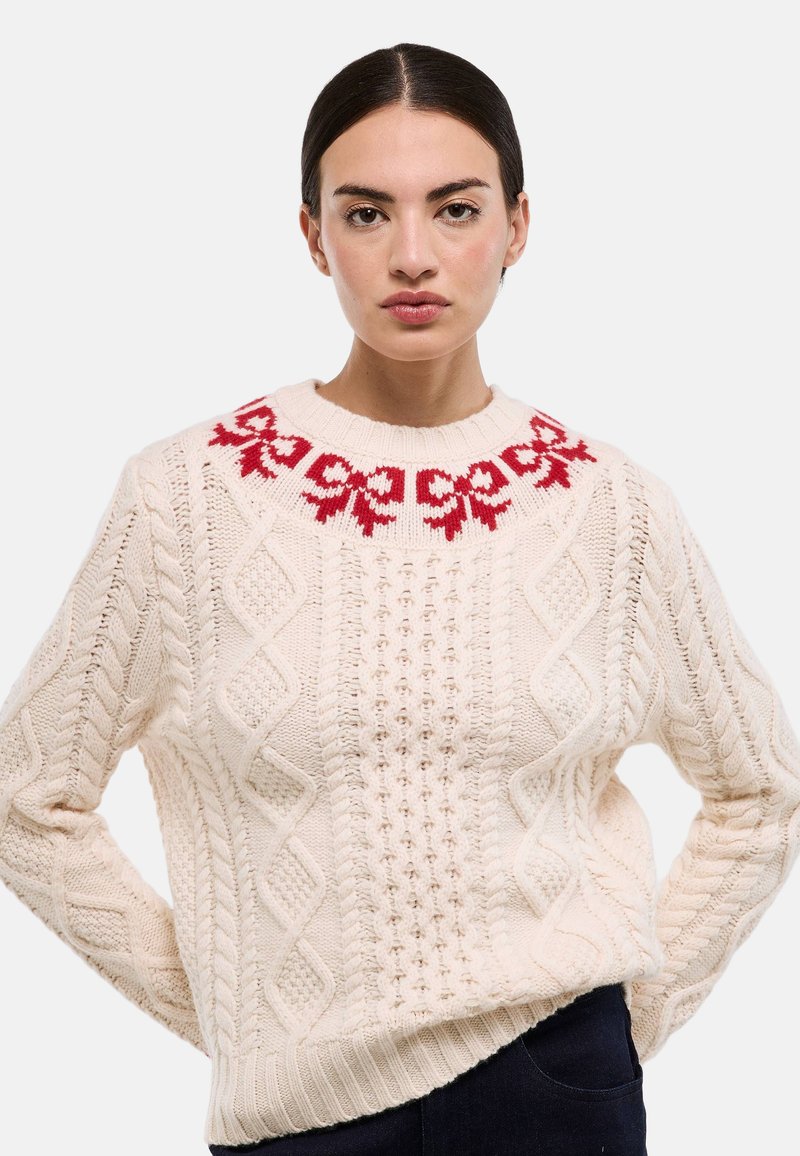 Pull en maille crème avec un col rond, un motif floral rouge au niveau du col et un design texturé en tricot torsadé sur toute la surface.