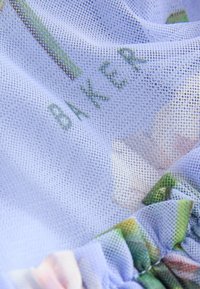 White mesh fabric with visible "BAKER" text beneath, featuring gathered edges with pastel floral print details.