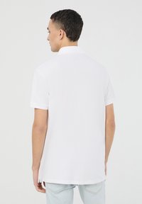 Polo bianco a maniche corte con colletto, caratterizzato da una linea dritta e sottili spacchi ai lati. Texture morbida e design minimalista.