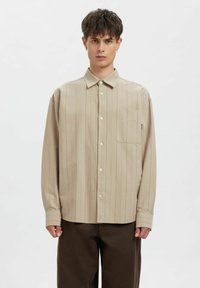 Beige skjorte med knapper og vertikale striper i lysere nyanser. Har krage, lange ermer og en enkelt brystlomme.