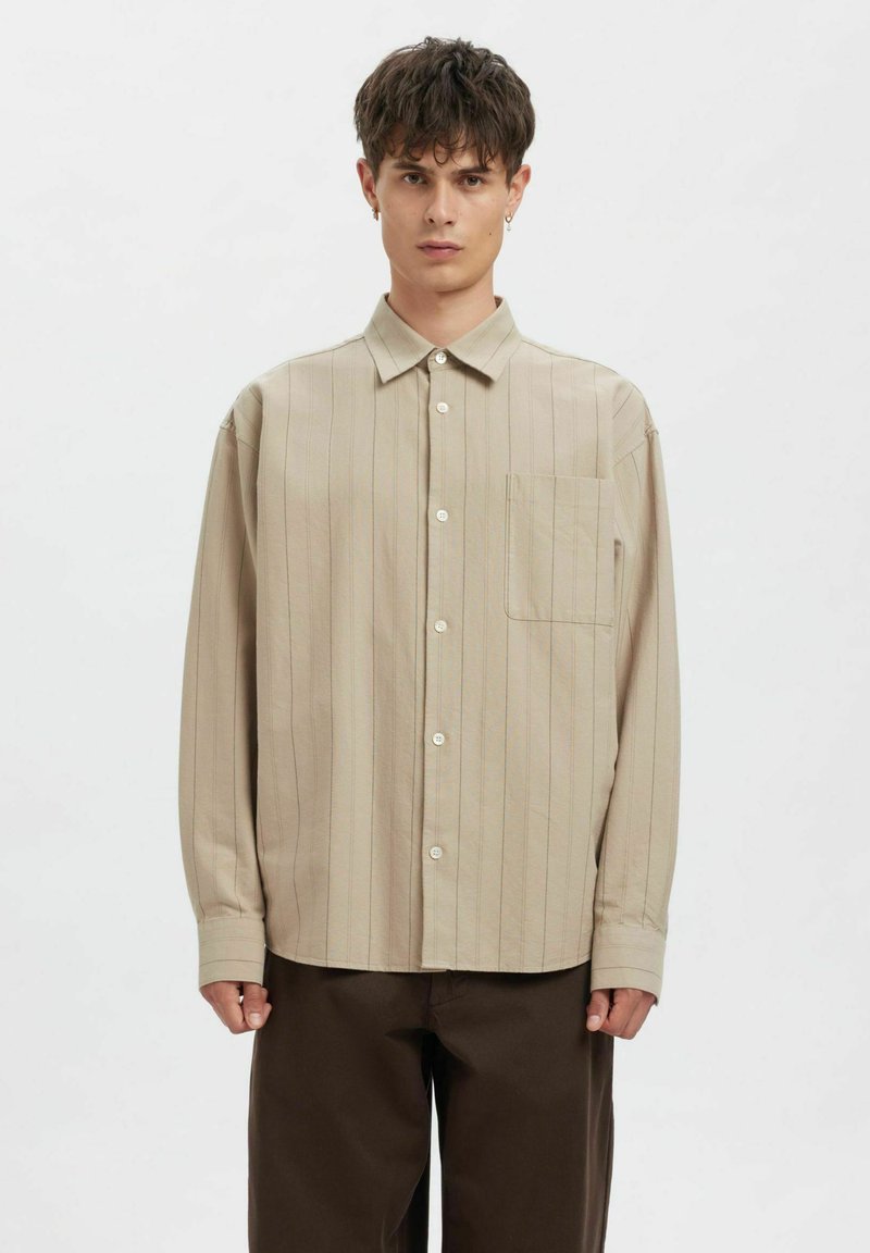 Beige skjorte med knapper og vertikale striper i lysere nyanser. Har krage, lange ermer og en enkelt brystlomme.