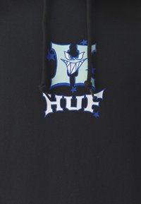 Svart hoodie med en grafisk tryck som har en stiliserad bokstav 'H' i ljusblått och ett karikatyraktigt ansikte med tänder, omritat i mörkblått.