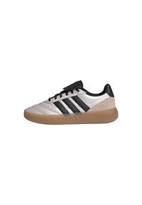 Zapatilla deportiva beige claro con detalles en negro, que cuenta con una parte superior de cuero liso, tres rayas negras y una suela de goma beige texturizada.