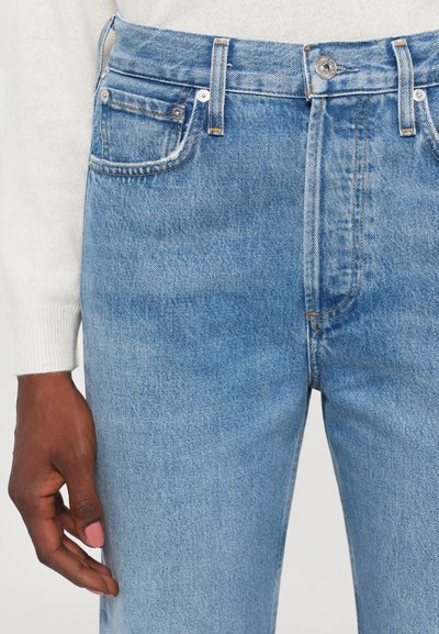 Light blue denim jeans with a straight cut, featuring a button fly, five pockets, and stitched detailing along the seams.