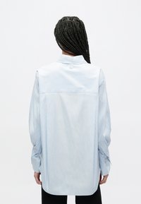 Jasnoniebieska koszula w paski z kołnierzykiem na guziki, o luźnym kroju, z długimi rękawami i zaokrąglonym dołem. Wykonana z gładkiej tkaniny.