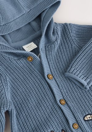 Blauer gestrickter Baby-Cardigan mit Kapuze, ausgestattet mit Holzknöpfen und bestickten Augen auf der Vorderseite. Strukturierter Stoff und gerippte Bündchen.