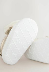 Goldene Sneaker mit einer strukturierten Oberseite, weißen Gummisohlen mit einem Diamantmuster und Klettverschlussriemen zum Verschließen.
